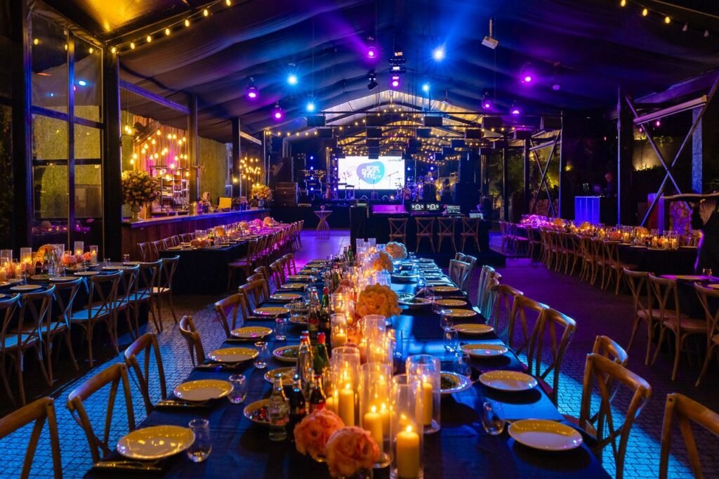 Luxurious evening event setup with candlelit tables and vibrant lighting in a spacious venue.