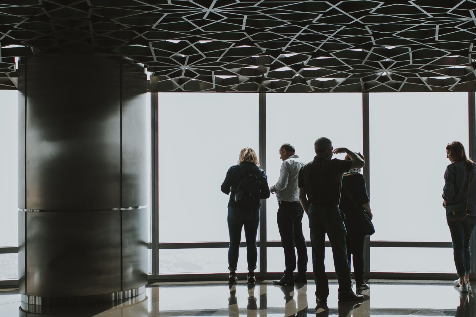 Group of people viewing cityscape through large glass windows in a Dubai skyscraper. Modern architecture and urban exploration.